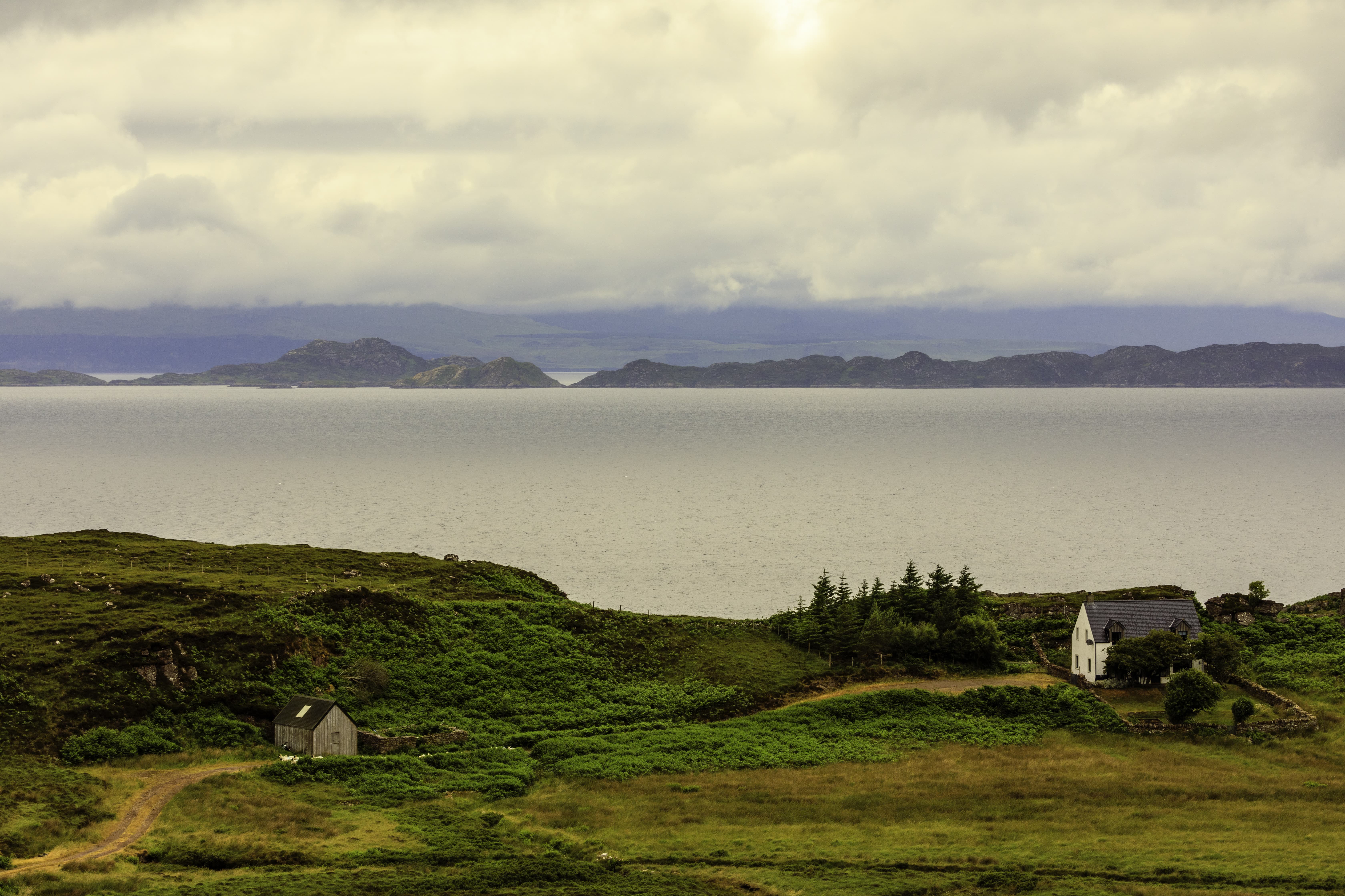 A tranquil view over a Scottish loch, where the calm waters mirror the overcast sky, creating a scene of peaceful reflection.