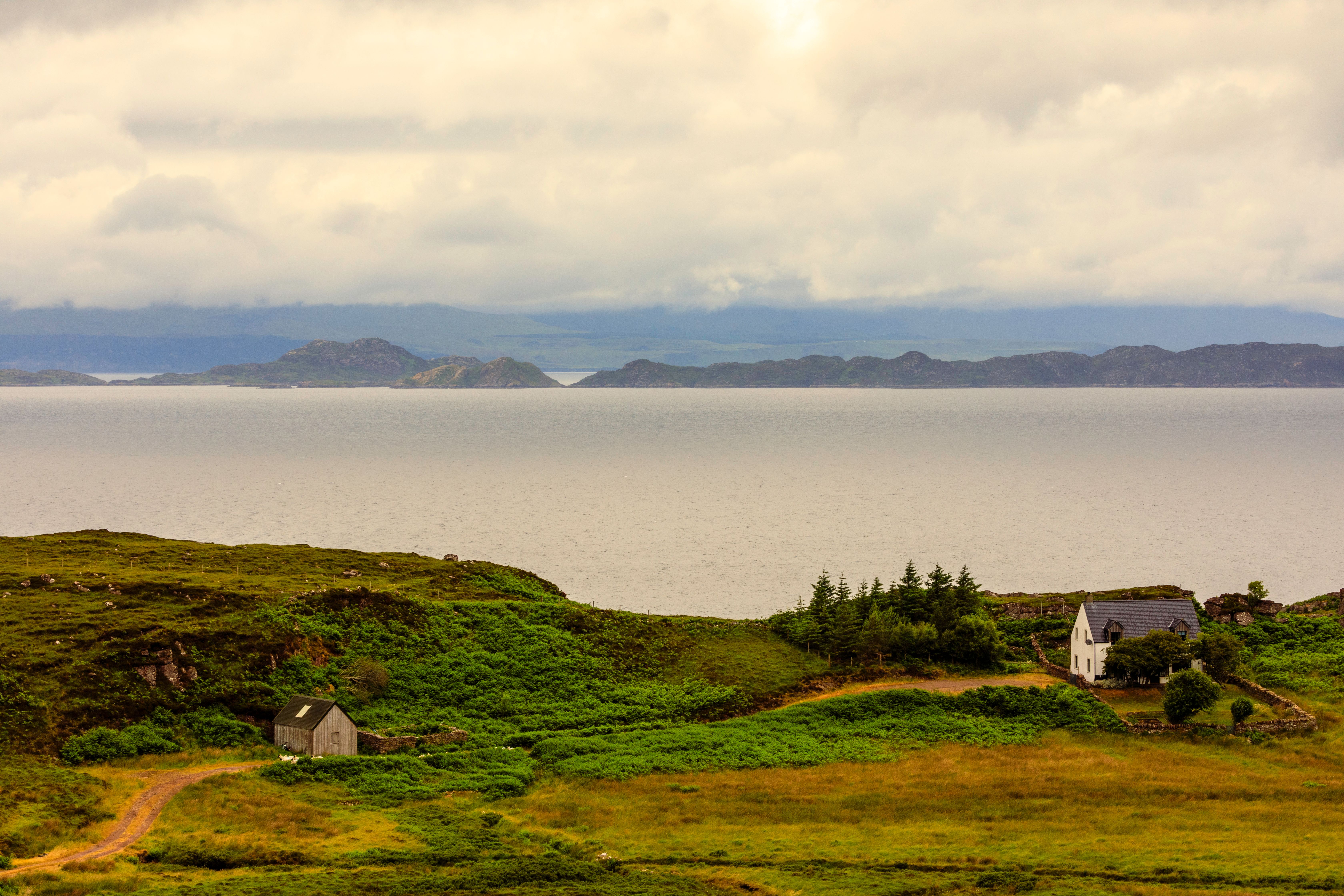 A tranquil view over a Scottish loch, where the calm waters mirror the overcast sky, creating a scene of peaceful reflection.