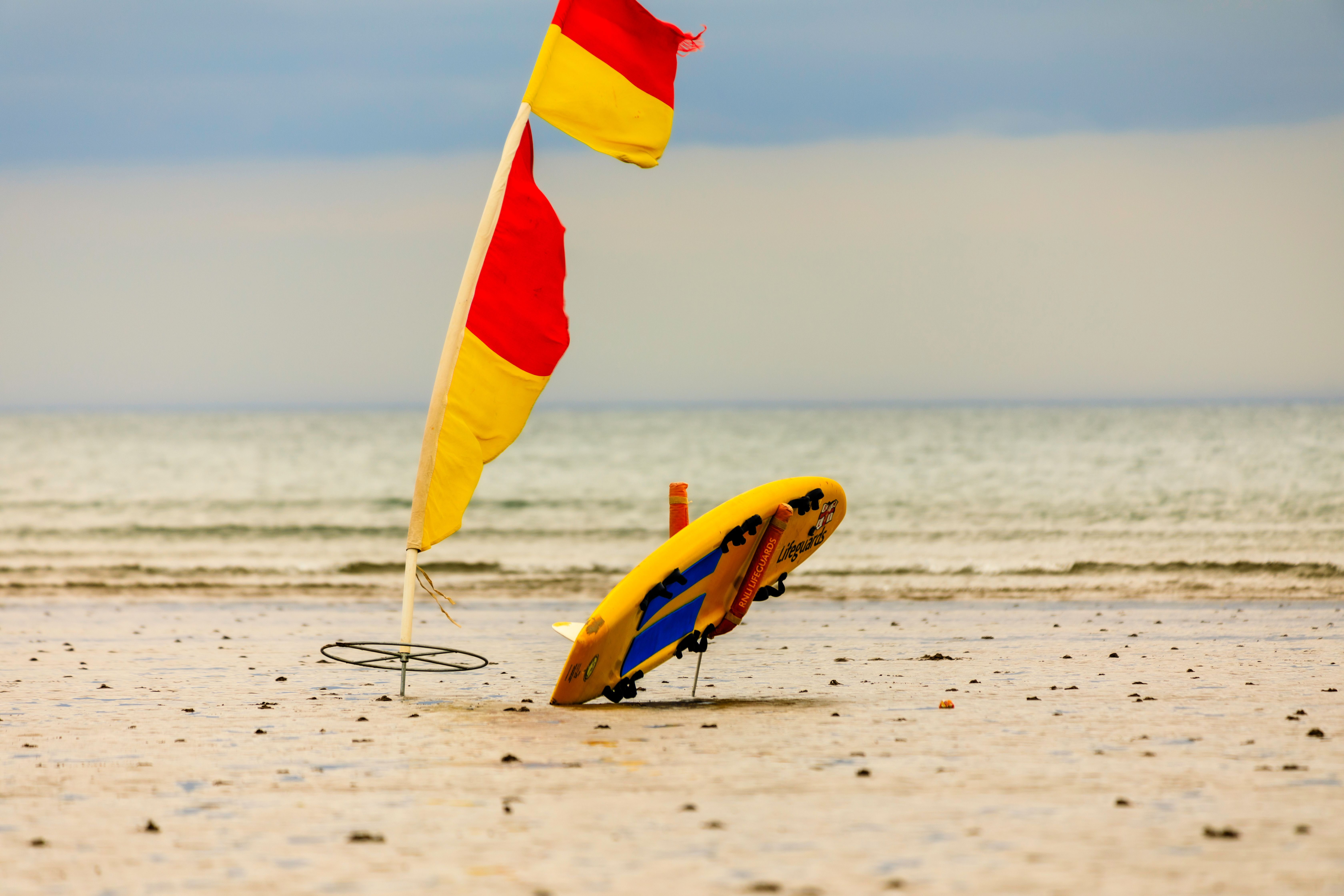 Brightly colored flags mark the coastline, their vibrant hues standing out against the muted tones of the sandy beach and overcast sky.