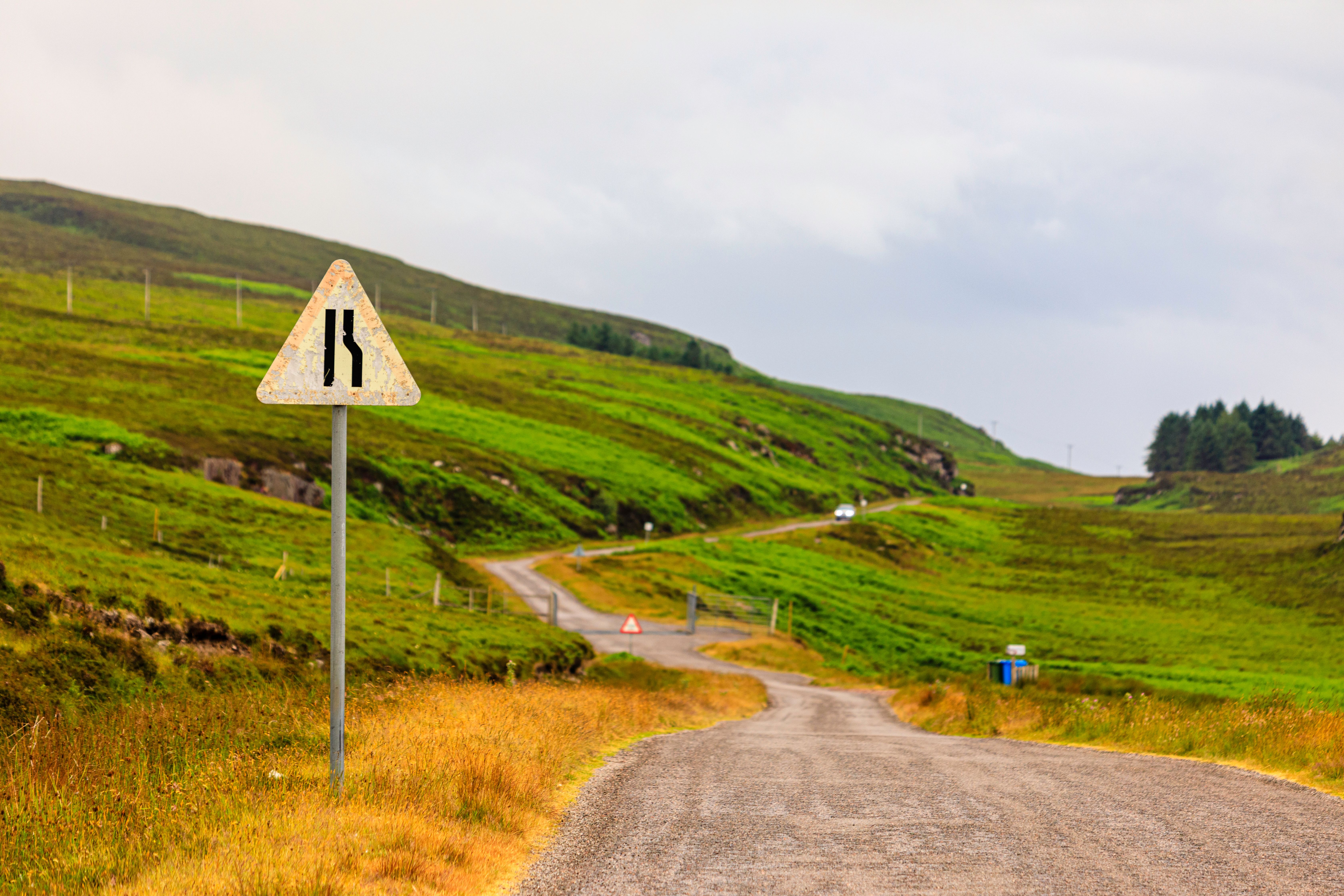 An old roadsign signals a winding path through the lush, green Highlands, inviting travelers to explore the scenic routes of Scotland.